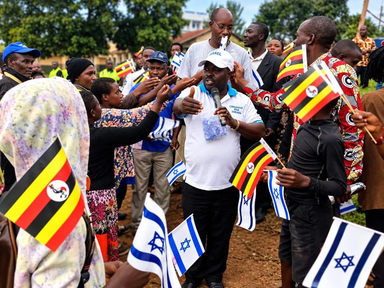 A crowd waving Ugandan and Israeli flags